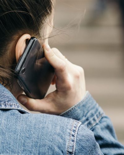 Close-up over the shoulder young woman talking on the black mobile phone on the street.